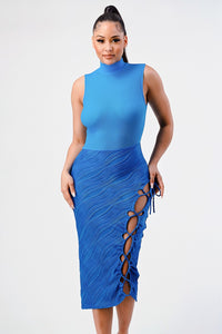 vibrant blue sleeveless midi dress with a high neckline, featuring a textured top and a skirt with a unique wave pattern. The dress includes an eye-catching side slit adorned with a lace-up detail and tassel ties, set against a simple backdrop to highlight its striking design. Rêve Dorés