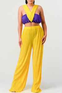 Introducing the "Sunset Fiesta Two-Piece Set," a vibrant and eye-catching set that captures the essence of a perfect sunset. This exquisite pair consists of a pleated bandeau-style crop top in a deep purple hue, designed with a twist at the bust for a touch of elegance. The top is complemented by high-waisted, wide-leg pants in a brilliant yellow, exuding warmth and joy.