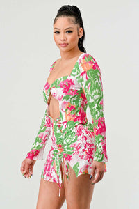 Twist-Front Floral Cut-Out Dress: A stylish mini dress with a twist-front cut-out at the bust, featuring a bright floral print in pink, green, and white. The dress has long sleeves and side ruching with a drawstring.