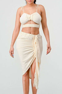 Cream Dream Ruched Set: Soft cream crop top with adjustable spaghetti ties and charming bow detail, paired with a high-waisted midi skirt featuring flattering ruching and playful fringe tassels.