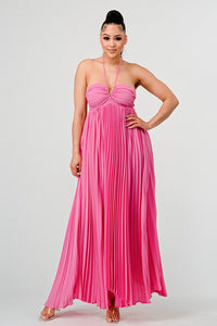 Sleeveless silhouette ideal for warm weather occasions Model wearing a flowing pink halter-neck maxi dress with a ruched bodice and pleated skirt. The elegant, airy design creates a graceful silhouette, perfect for formal events, summer gatherings, or beach weddings -  Rêve Dorés