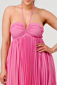 Rêve Dorés Model wearing a flowing pink halter-neck maxi dress with a ruched bodice and pleated skirt. The elegant, airy design creates a graceful silhouette, perfect for formal events, summer gatherings, or beach weddings. Stretchable fabric with elastic back ensures a comfortable and flexible fit