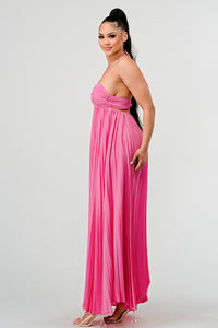 Rêve Dorés Model wearing a flowing pink halter-neck maxi dress with a ruched bodice and pleated skirt. The elegant, airy design creates a graceful silhouette, perfect for formal events, summer gatherings, or beach weddings. Stretchable fabric with elastic back ensures a comfortable and flexible fit