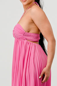 Rêve Dorés Model wearing a flowing pink halter-neck maxi dress with a ruched bodice and pleated skirt. The elegant, airy design creates a graceful silhouette, perfect for formal events, summer gatherings, or beach weddings. Stretchable fabric with elastic back ensures a comfortable and flexible fit