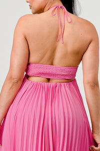 Rêve Dorés Model wearing a flowing pink halter-neck maxi dress with a ruched bodice and pleated skirt. The elegant, airy design creates a graceful silhouette, perfect for formal events, summer gatherings, or beach weddings. Stretchable fabric with elastic back ensures a comfortable and flexible fit