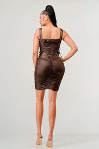 Shirring Detail PU Mini Dress - Model wearing a sleek brown ruched mini dress featuring adjustable straps with buckle details and side ties. The form-fitting silhouette and leather-like texture create a bold and edgy look, perfect for a night out or statement-making occasions. Rêve Dorés