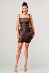 Shirring Detail PU Mini Dress - Model wearing a sleek brown ruched mini dress featuring adjustable straps with buckle details and side ties. The form-fitting silhouette and leather-like texture create a bold and edgy look, perfect for a night out or statement-making occasions. Rêve Dorés