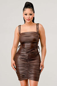 Shirring Detail PU Mini Dress - Model wearing a sleek brown ruched mini dress featuring adjustable straps with buckle details and side ties. The form-fitting silhouette and leather-like texture create a bold and edgy look, perfect for a night out or statement-making occasions. Rêve Dorés