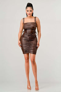 Shirring Detail PU Mini Dress - Model wearing a sleek brown ruched mini dress featuring adjustable straps with buckle details and side ties. The form-fitting silhouette and leather-like texture create a bold and edgy look, perfect for a night out or statement-making occasions. Rêve Dorés