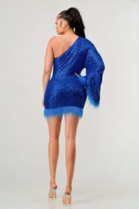 Model wearing a dazzling one-shoulder mini dress in vibrant blue, covered in shimmering sequins and featuring a dramatic single sleeve. The hem and sleeve are accented with matching feathered trim, creating a bold and luxurious look ideal for parties and special occasions - Rêve Dorés