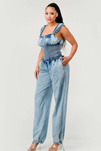 Model wearing a unique denim halter romper featuring a deep V-neckline, frayed edges, and bold orange rope detailing styled in abstract patterns across the bodice and shorts. The playful design combines edgy and artistic elements, perfect for making a bold fashion statement. Rêve Dorés