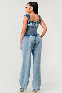 Model wearing a unique denim halter romper featuring a deep V-neckline, frayed edges, and bold orange rope detailing styled in abstract patterns across the bodice and shorts. The playful design combines edgy and artistic elements, perfect for making a bold fashion statement. Rêve Dorés