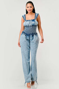 Model wearing a unique denim halter romper featuring a deep V-neckline, frayed edges, and bold orange rope detailing styled in abstract patterns across the bodice and shorts. The playful design combines edgy and artistic elements, perfect for making a bold fashion statement. Rêve Dorés