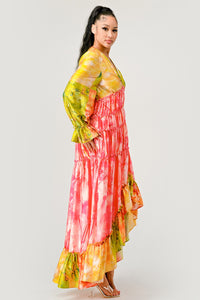 Sunset Breeze Tiered Maxi Dress | Model wearing a vibrant bohemian-style maxi dress with a colorful tie-dye pattern in shades of yellow, pink, and green. Featuring a deep V-neckline, tiered ruffle detailing, and a high-low hem, this dress exudes a carefree and whimsical vibe, perfect for summer events or festivals. Rêve Dorés