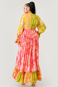 Sunset Breeze Tiered Maxi Dress | Model wearing a vibrant bohemian-style maxi dress with a colorful tie-dye pattern in shades of yellow, pink, and green. Featuring a deep V-neckline, tiered ruffle detailing, and a high-low hem, this dress exudes a carefree and whimsical vibe, perfect for summer events or festivals. Rêve Dorés