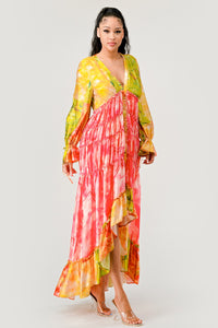 Sunset Breeze Tiered Maxi Dress | Model wearing a vibrant bohemian-style maxi dress with a colorful tie-dye pattern in shades of yellow, pink, and green. Featuring a deep V-neckline, tiered ruffle detailing, and a high-low hem, this dress exudes a carefree and whimsical vibe, perfect for summer events or festivals. Rêve Dorés