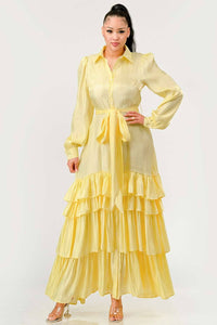 Yellow Tiered Ruffle Maxi Dress with Belt: A bright yellow dress featuring a button-up front, tiered ruffle skirt, and a matching fabric belt at the waist. The dress has long, puffed sleeves and a collared neckline. Rêve Dorés