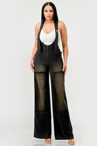 Urban Noir Denim Overalls Black Jumpsuit. Rêve Dorés Model wearing a stylish black denim overall jumpsuit featuring wide-leg pants, adjustable straps, and a front zipper closure. Paired with a white fitted tank top, this outfit offers a chic and modern twist on classic overalls, perfect for casual yet trendy looks.