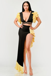 Sunset Ruffle Glamour Gown - Model wearing a sophisticated black and yellow evening gown featuring a plunging neckline with a silver ring accent, a high side slit, and ruffled yellow details cascading along the shoulders and hem. Perfect for elegant summer events or formal occasions. Rêve Dorés