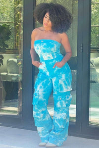 Rêve Dorés Blue Tie Dye Strapless Utility Jumpsuit | Model wearing a vibrant strapless blue tie-dye jumpsuit featuring a button-up front, wide-leg design, and multiple utility-style pockets. The relaxed fit and bold pattern make it a stylish choice for casual outings or summer events.