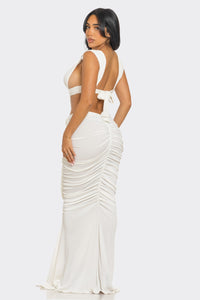 Sahara Mystique Pleated Gown - Model wearing a stunning beige cutout maxi dress featuring a plunging neckline, circular ring accents, and intricate ruched detailing throughout. The floor-length design with a figure-hugging silhouette exudes elegance and bold sophistication, perfect for an upscale evening event. - Rêves Dorés