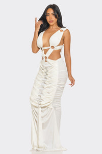 Sahara Mystique Pleated Gown - Model wearing a stunning beige cutout maxi dress featuring a plunging neckline, circular ring accents, and intricate ruched detailing throughout. The floor-length design with a figure-hugging silhouette exudes elegance and bold sophistication, perfect for an upscale evening event. - Rêves Dorés