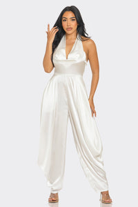 Rêve Dorés Ivory Serenity Jumpsuit | Model wearing an elegant white satin jumpsuit featuring a halter neckline with a draped cowl detail and a flowy silhouette. The sophisticated design exudes timeless glamour, perfect for formal occasions or special eventsATHINA