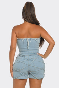 Sweet Heart Neck Line Romper | Model wearing a trendy strapless denim romper featuring a sweetheart neckline with frayed detailing, a button-up front, and ruched accents along the waist and shorts. This chic and playful outfit is perfect for casual outings or summer events by Rêve Dorés