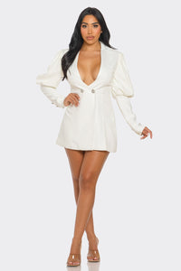 Model wearing a chic white blazer-style mini dress featuring a deep V-neckline, structured shoulders, puffed long sleeves, and decorative rhinestone buttons for a sophisticated and elegant look - Rêve Dorés