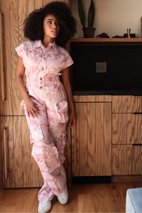 Model wearing a pink utility-style jumpsuit featuring a button-up front, short sleeves, and cargo pockets for a functional yet stylish look. The relaxed fit and soft tie-dye pattern make it perfect for casual outings or chic everyday wear by Rêve Dorés