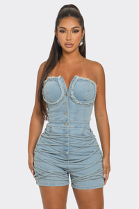 Sweet Heart Neck Line Romper | Model wearing a trendy strapless denim romper featuring a sweetheart neckline with frayed detailing, a button-up front, and ruched accents along the waist and shorts. This chic and playful outfit is perfect for casual outings or summer events by Rêve Dorés