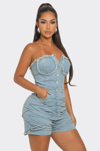 Sweet Heart Neck Line Romper | Model wearing a trendy strapless denim romper featuring a sweetheart neckline with frayed detailing, a button-up front, and ruched accents along the waist and shorts. This chic and playful outfit is perfect for casual outings or summer events by Rêve Dorés